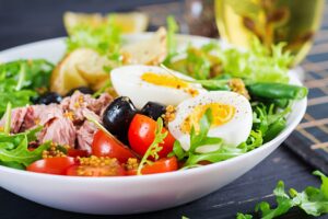 healthy hearty salad tuna green beans tomatoes eggs potatoes black olives close up bowl table